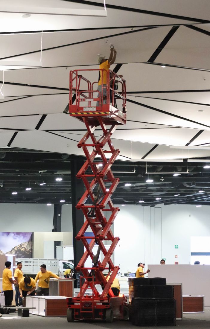 Plataforma de tijera elevada a gran altura mientras un técnico instala en el techo de un salón